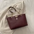 Large burgundy tote bag with gold chain strap and deer pendant on a beige suit - Red