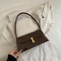 Dark brown patent leather baguette bag with gold buckle on a stylish suit backdrop - Brown