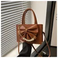 Détail du sac en cuir caramel avec un grand nœud et une chaîne décorative en perles - Marron