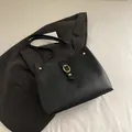 Classic black leather tote bag with gold oval buckle on a dark grey blazer background - Black