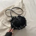 Minimalist black suede drawstring bucket bag with a chunky braided handle and crossbody strap - Black