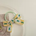 Détail d'un chouchou vert avec nœud à carreaux jaunes et broderie florale douce - Jaune
