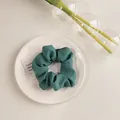 Détail d'un chouchou en tissu plissé vert foncé posé sur une assiette blanche - Texturé Vert Foncé