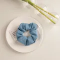 Détail d'un chouchou bleu Morandi en tissu gaufré posé sur une assiette en céramique - Texturé Bleu Clair