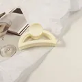 Détail d'une pince à cheveux mate crème avec design en arc arrondi sur fond épuré - Blanc Cassé