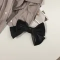Détail d'une barrette à cheveux nœud noir en satin sur une chemise et un magazine - Noir