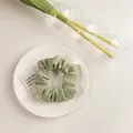 Détail d'un chouchou vert sauge en tissu gaufré posé sur une assiette blanche élégante - Texturé Vert Clair