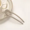 Minimalistische U-förmige Haarnadel in Matt-Mocha auf cremefarbenem Lifestyle-Hintergrund - Grau