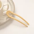 Detail einer matt beigen U-förmigen Haarnadel für Damen auf minimalistischer Keramik - Milchgelb