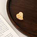 Detail of a mini heart-shaped acetate hair claw featuring orange and white checkerboard pattern - Orange and White Grid