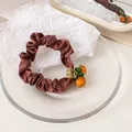 Detail shot of brown satin scrunchie with a cute orange pendant in a glass tray - Dark Brown
