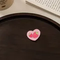Detail eines rosa Acryl-Herzclips mit Erdbeer-Stickerei auf einem Holztablett - Erdbeere Herz