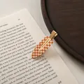 Detail of checkered orange and white acetate hair clip placed on a vintage book page - Small / Orange White Plaid