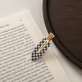 Detail of checkered acetate hair clip with gold metal base placed on an open vintage book - Small / Black and White Plaid