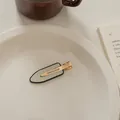 Detail der hellgrünen ovalen Haarspange mit schwarzem Rand auf weißem Keramikteller - Spurenloser Clip-Weiß