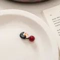 Detail of cute cartoon girl hair clip with red bead on white ceramic plate with book - Black Hair Red Bead