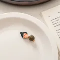 Detail of a cute cartoon girl hair clip with a green bead on a white ceramic plate - Bun Hairstyle