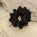 Detailweergave van de pluizige zwarte scrunchie op beige stoffen achtergrond - Zwart