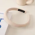 Detail eines beigen Strickstirnbands mit handgefertigtem Etikett auf weichem Stoff - Cremeweiß