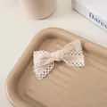 Détail d'une pince à cheveux nœud en dentelle crème avec texture ajourée sur plateau - Crème