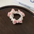 Détail de l'élastique à perles avec nœuds en satin rose sur un fond en bois texturé - Rose