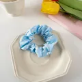 Detail eines hellblauen Scrunchie mit weißen Gänseblümchen auf einem Keramikteller - Hellblau