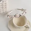 Detail of cream satin headband with black-edged bows on a ceramic coffee cup - Cream White Bow (Contrast Black Edge) / White