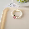 Primer plano de un coletero de satén blanco crema con un lindo colgante de melocotón rosa - Scrunchie de Melocoton