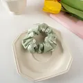 Detailed close-up of a light green floral scrunchie with white daisy prints on a ceramic plate - Green