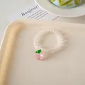 Close-up of a clear spiral hair tie featuring a cute pink peach charm with green leaves - Peach Telephone Cord Hair Tie