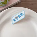 Détail d'une broche en acrylique blanc avec texte bleu et icône de lunettes stylée - Style artistique