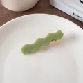 Detail of wavy green acetate hair clip on a white ceramic plate with a gold metal base - Matcha Green