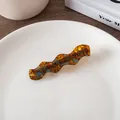 Close-up of wavy acetate hair clip with tortoise shell texture on a white ceramic plate - Glazed Multi-color