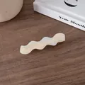 Close-up of wavy acetate hair clip in pearl white finish on a minimalist background - Pearl White