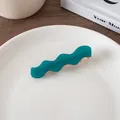 Close-up of a teal wave-shaped acetate hair clip with golden metal fastener on a plate - Lake Blue