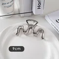 Détail d'une pince à cheveux vague en métal argenté de 9cm sur une assiette blanche - Forme M-Argent