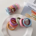 Bunte Makronen-Haargummis im Set mit Klarsichtdose auf einem weißen Keramikteller - Macaron-Farbe Basic-Stil