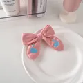 Dettaglio di un fermaglio a fiocco rosa con cigni blu ricamati su un piatto bianco - 37# Cigno - Rosa Intenso