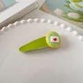 Dettaglio di un simpatico fermaglio per capelli verde con motivo busta a cuore su un piatto - Verde Busta
