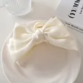 Detalle de una pinza para el pelo grande de satén crema con lazo sobre un plato blanco - crema