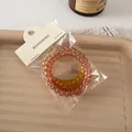 Dettaglio di due elastici a spirale color ambra e marrone su vassoio beige testurizzato - Arancione Scuro E Marrone