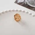 Close-up of a small golden metal smiley face hair claw clip on a white ceramic tray - Happy Face - Gold