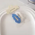 Detailansicht welliger Haarklammern in Blau und Weiß auf einer minimalistischen Karte - Weiß + Blau