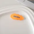 Detail einer orangefarbenen Haarklammer in Wolkenform auf einem weißen Keramiktablett - Orange