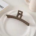 Detalle de una pinza de pelo mate color café oscuro sobre un plato de cerámica blanca - Estilo Barra / Café Oscuro