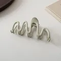 Macro shot of large sage green matte claw clip with elegant wavy design on books - Sage Green