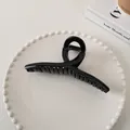 Glossy black hair claw clip with a twisted minimalist design on a white ceramic tray - Large Cross Style (7#)