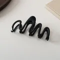Macro detail of wave-shaped matte black hair claw clip with minimalist textured finish - Black