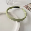 Close-up of light green padded fabric headband with a handmade label on a white table - Green
