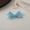 Gros plan détaillé d'une pince à cheveux en satin bleu clair à double nœud sur fond texturé - Bleu Ciel